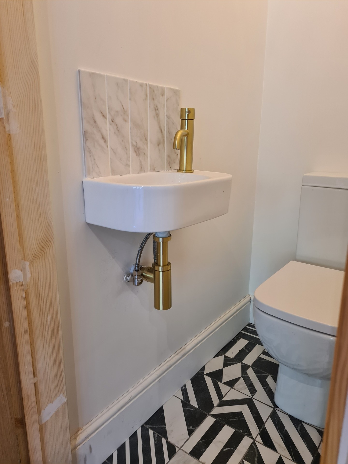 Wall-hung basin with gold tap and marble splashback in cloakroom