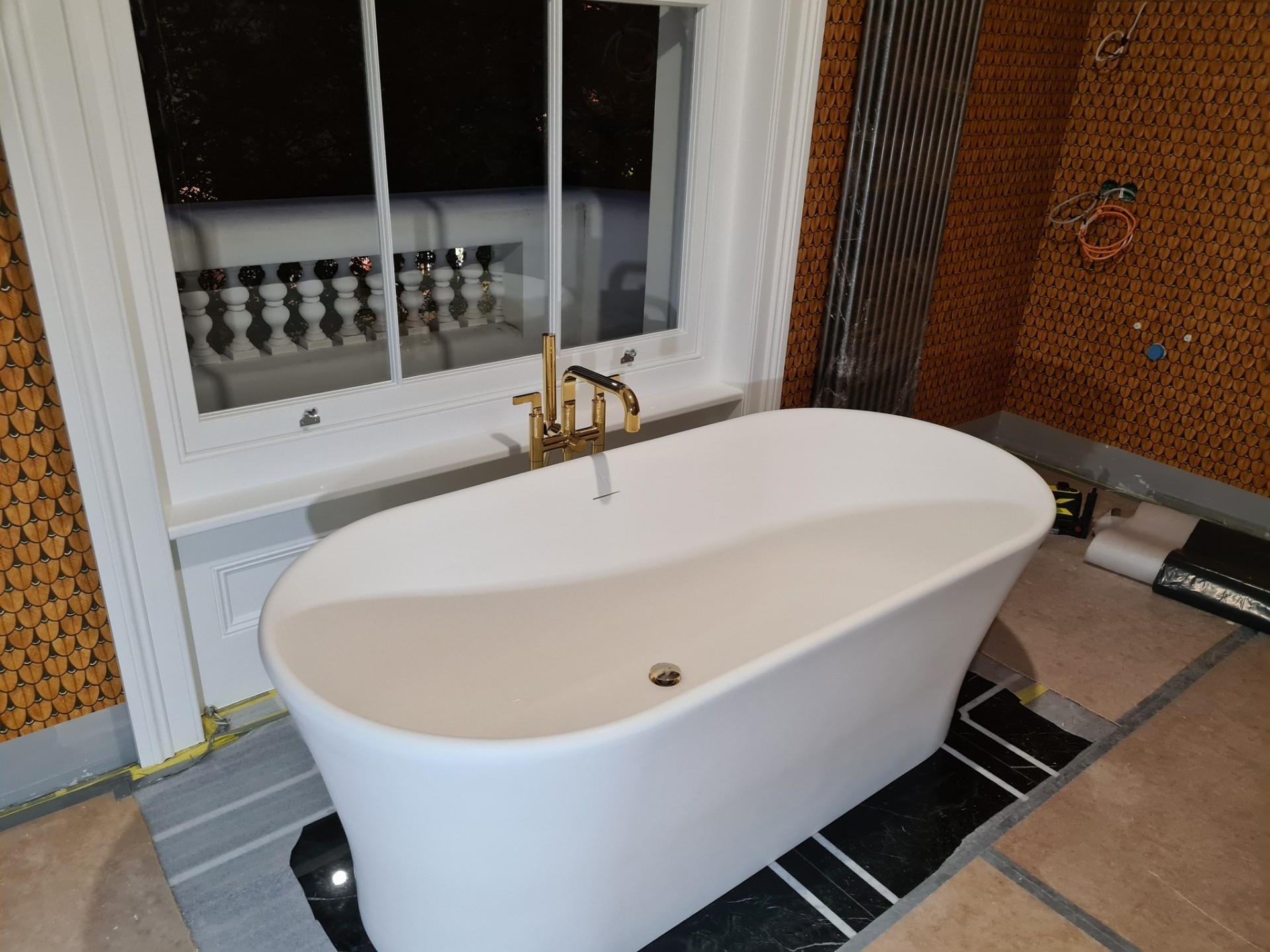 Freestanding bath with gold mixer tap installed in luxury bathroom with penny tiles