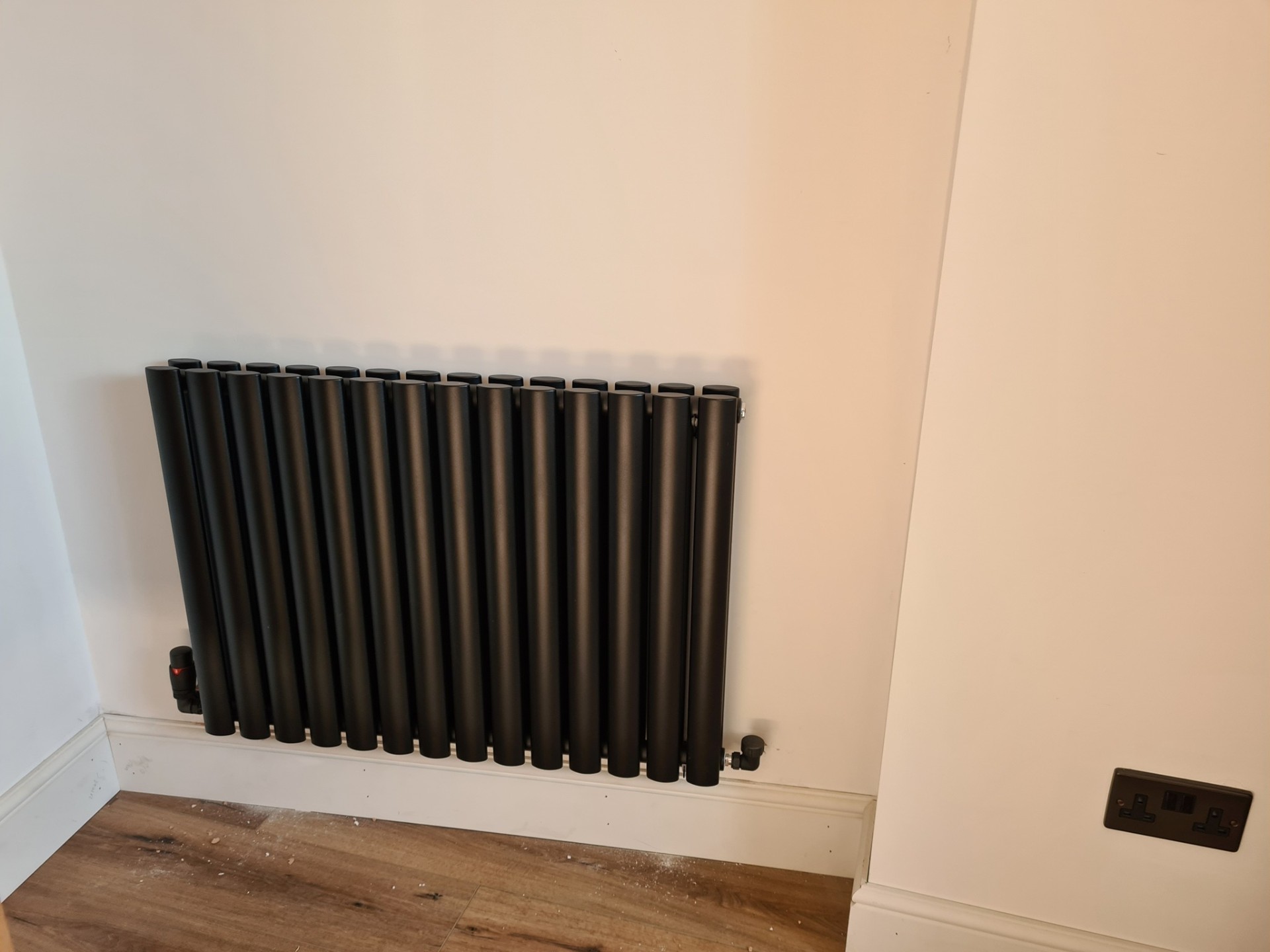 Horizontal anthracite column radiator installed above oak flooring