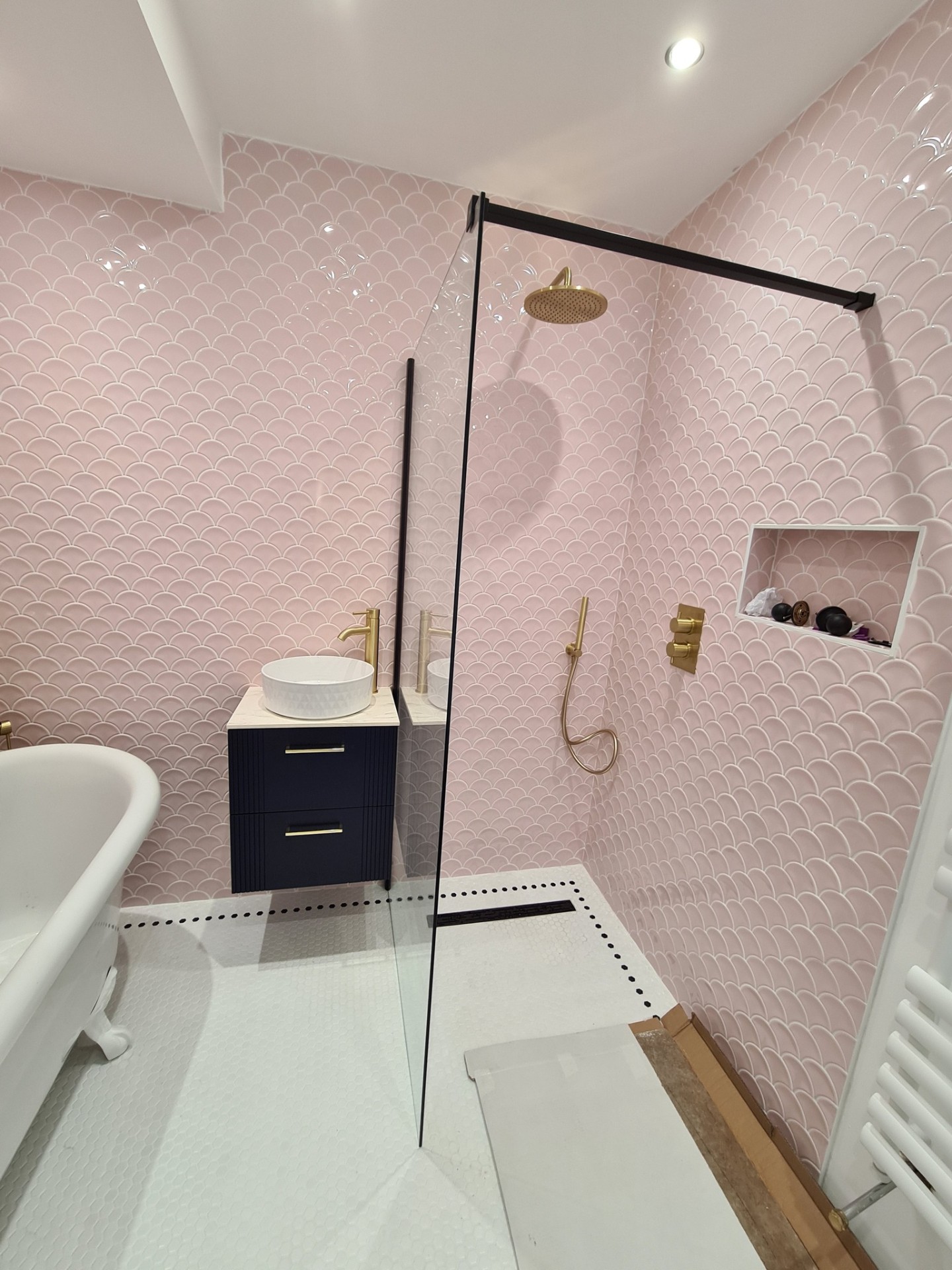 Walk-in shower with brass rainfall head, navy vanity unit and pink scallop tiles