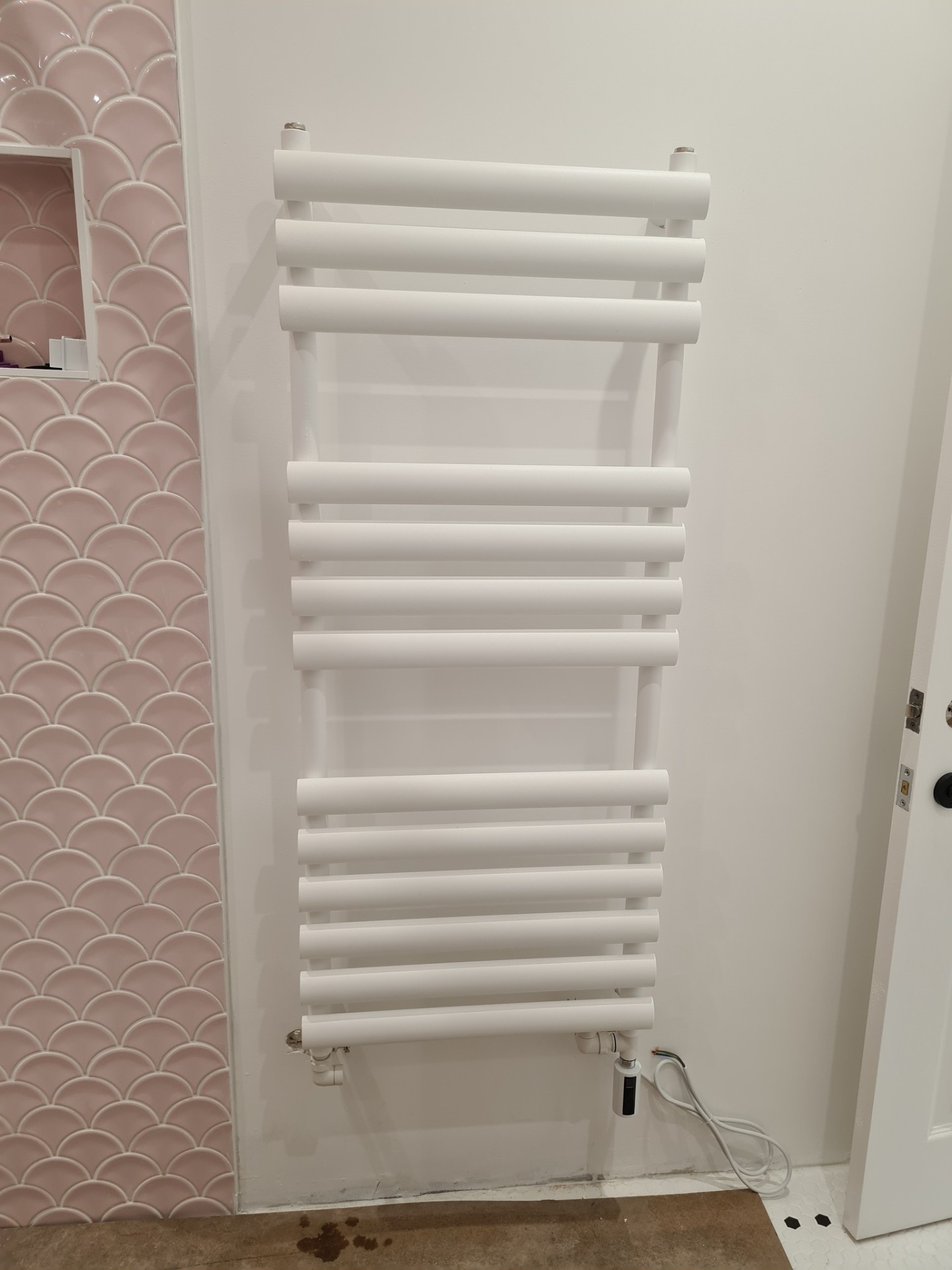 White heated towel rail installed next to pink scallop tiled bathroom